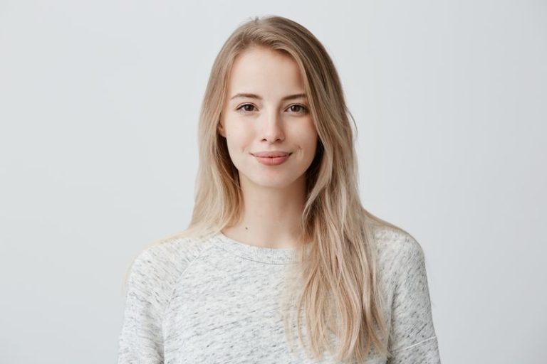 Pretty smiling joyfully female with fair hair, dressed casually, looking with satisfaction at camera, being happy. Studio shot of good-looking beautiful woman isolated against blank studio wall